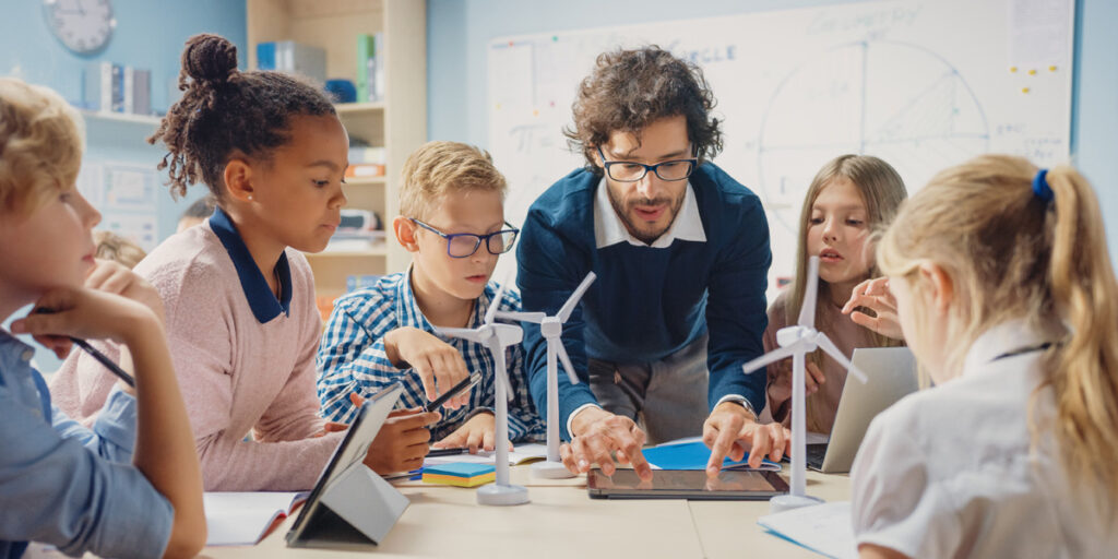 Kinder sitzen mit einem Lehrer vor Modell Windrädern